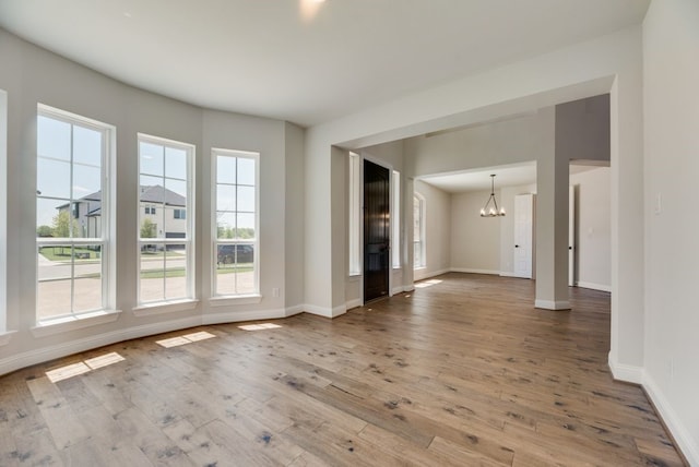 empty room with baseboards, a chandelier, and wood finished floors