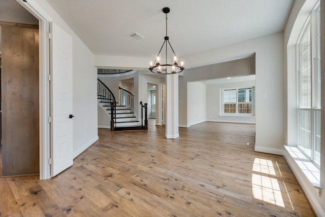 unfurnished dining area featuring a notable chandelier, stairs, visible vents, and hardwood / wood-style floors