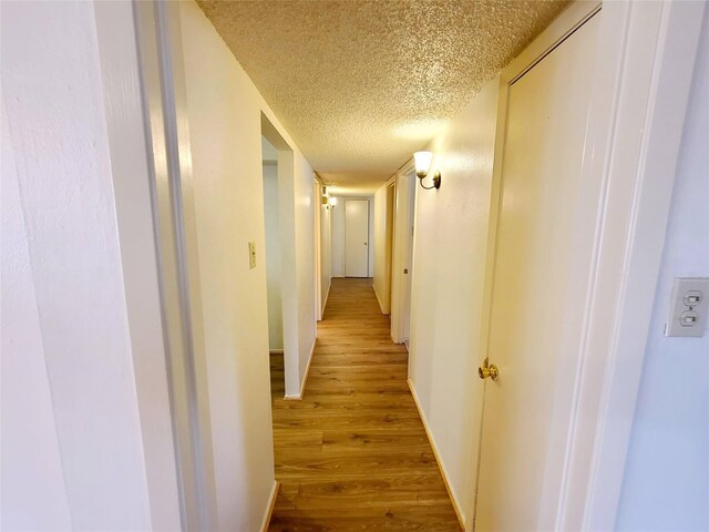 hallway with light hardwood / wood-style floors and a textured ceiling