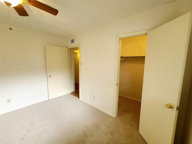 unfurnished bedroom featuring light carpet, a spacious closet, ceiling fan, and a closet