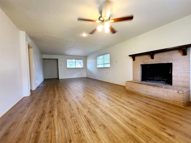 unfurnished living room featuring a textured ceiling, hardwood / wood-style flooring, a brick fireplace, and ceiling fan