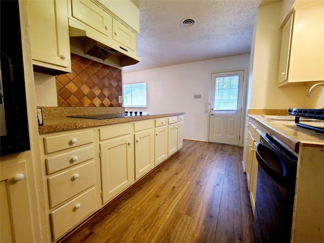 kitchen featuring black appliances, hardwood / wood-style flooring, decorative backsplash, and a textured ceiling