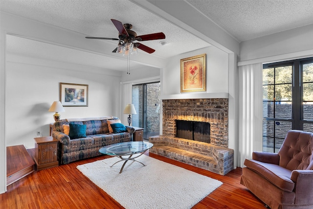 living room featuring hardwood / wood-style flooring, ceiling fan, a brick fireplace, and a textured ceiling