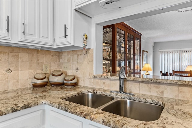 kitchen featuring sink, white cabinetry, tasteful backsplash, light stone counters, and a textured ceiling