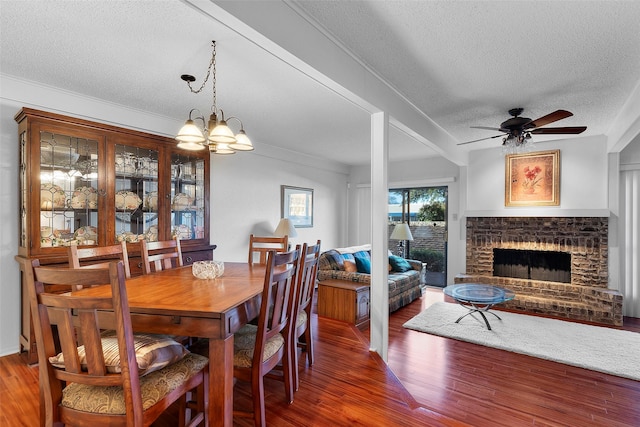 dining room with dark hardwood / wood-style flooring, a brick fireplace, ceiling fan with notable chandelier, and a textured ceiling