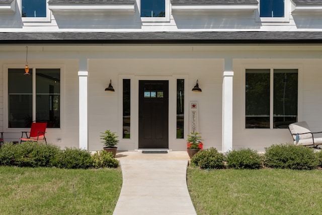 view of exterior entry with a lawn and covered porch