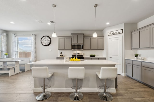 kitchen with sink, an island with sink, gray cabinets, pendant lighting, and appliances with stainless steel finishes