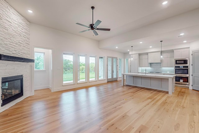 kitchen featuring light hardwood / wood-style floors, an island with sink, stainless steel appliances, a stone fireplace, and ceiling fan