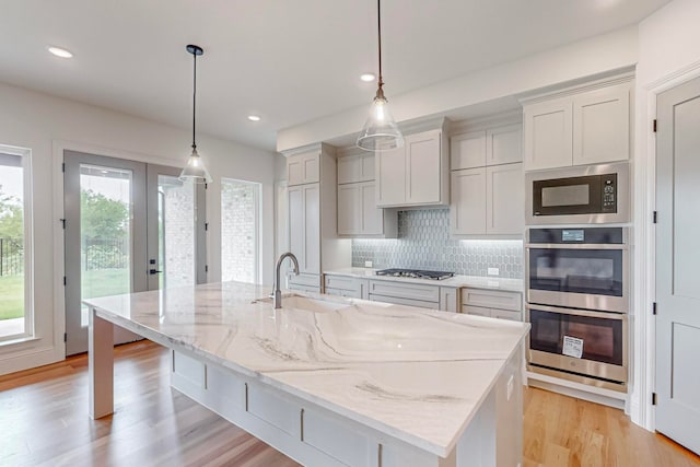 kitchen with appliances with stainless steel finishes, a center island with sink, sink, and decorative light fixtures