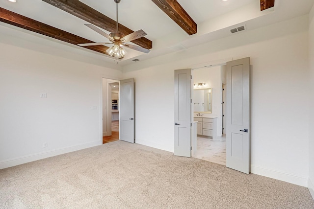 unfurnished bedroom featuring ceiling fan, light colored carpet, beamed ceiling, and ensuite bath