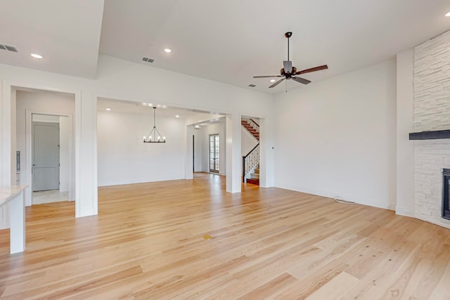 unfurnished living room featuring ceiling fan with notable chandelier, light wood-type flooring, and a stone fireplace