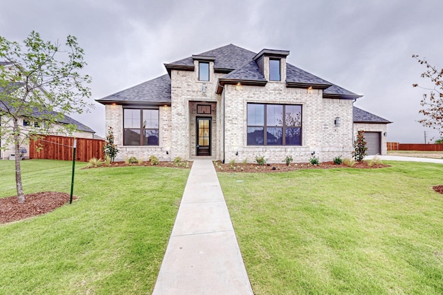 view of front of property with a shingled roof, an attached garage, fence, a front lawn, and brick siding