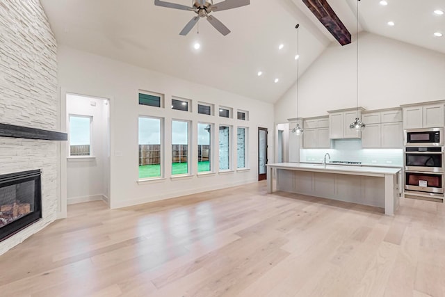 kitchen featuring ceiling fan, a stone fireplace, light hardwood / wood-style flooring, and hanging light fixtures