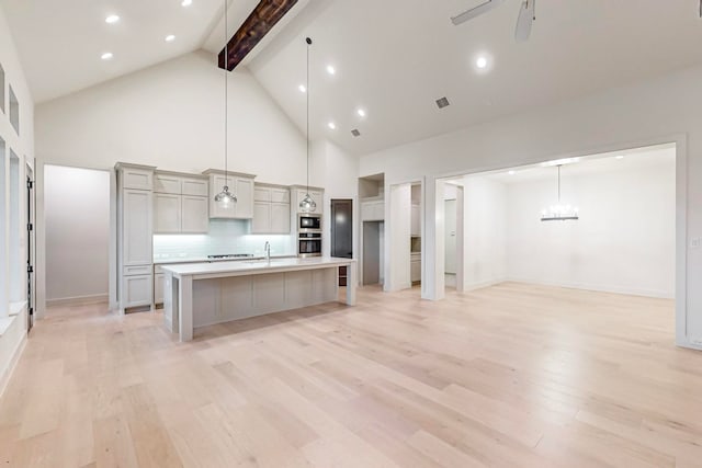 kitchen featuring a kitchen island with sink, hanging light fixtures, high vaulted ceiling, decorative backsplash, and light hardwood / wood-style flooring