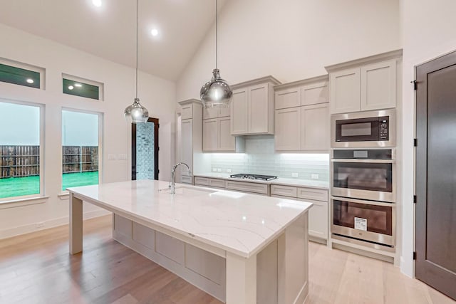 kitchen featuring light hardwood / wood-style floors, high vaulted ceiling, light stone countertops, decorative light fixtures, and sink