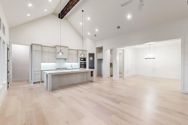 kitchen featuring a ceiling fan, an island with sink, gray cabinets, light countertops, and pendant lighting