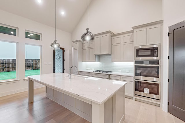 kitchen featuring light stone counters, a kitchen island with sink, a sink, hanging light fixtures, and appliances with stainless steel finishes