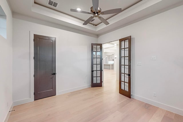 unfurnished room featuring a raised ceiling, light wood-type flooring, crown molding, ceiling fan, and french doors