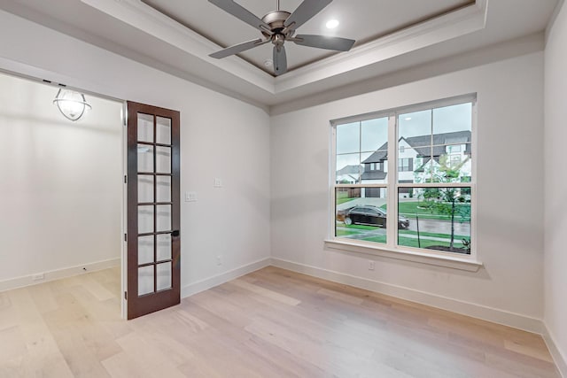 unfurnished room with light wood-style floors, baseboards, a raised ceiling, and a ceiling fan