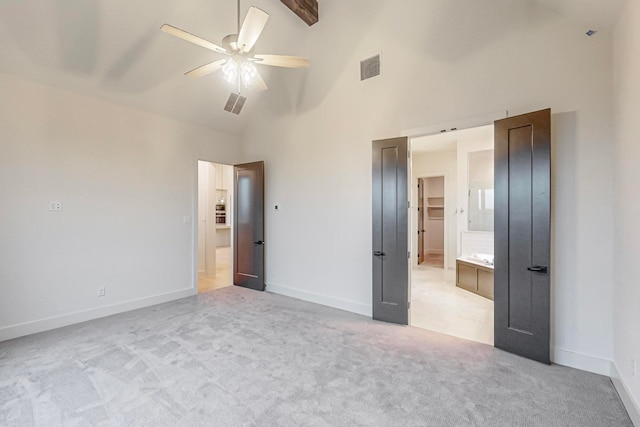 unfurnished bedroom with ensuite bath, ceiling fan, light colored carpet, and high vaulted ceiling