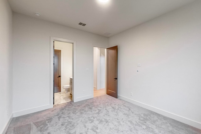 unfurnished bedroom featuring ensuite bath and light colored carpet