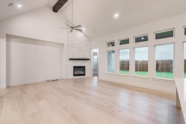 unfurnished living room featuring visible vents, light wood-style flooring, beamed ceiling, a fireplace, and high vaulted ceiling