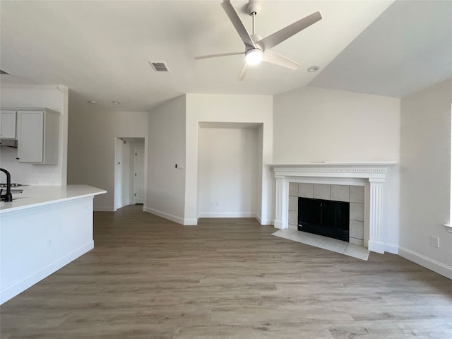 unfurnished living room featuring ceiling fan, a tile fireplace, vaulted ceiling, and light hardwood / wood-style flooring