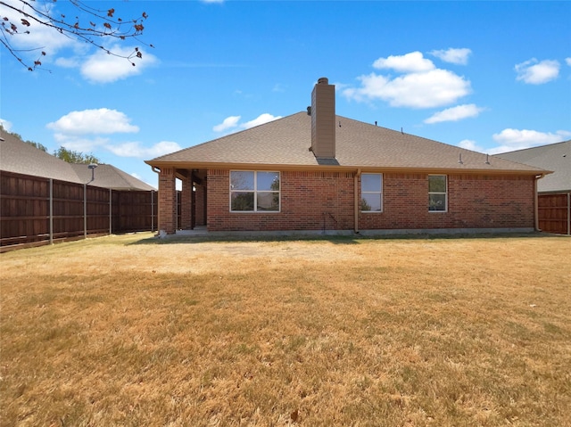 back of property featuring roof with shingles, brick siding, a chimney, a lawn, and a fenced backyard