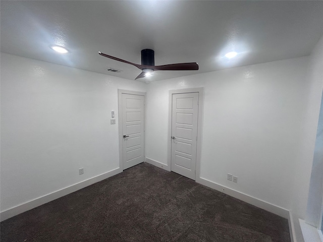 empty room with ceiling fan and dark colored carpet