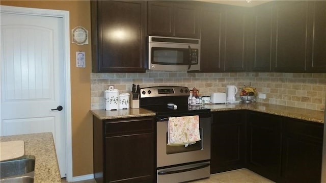 kitchen featuring dark brown cabinets, light stone countertops, stainless steel appliances, and tasteful backsplash