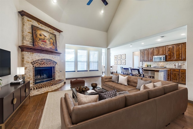 living room featuring high vaulted ceiling, dark wood-style flooring, a fireplace with raised hearth, and ceiling fan