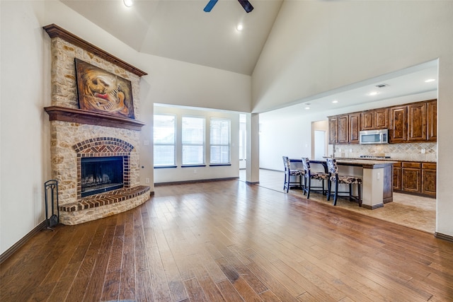 living room featuring ceiling fan, high vaulted ceiling, a fireplace, and hardwood / wood-style flooring