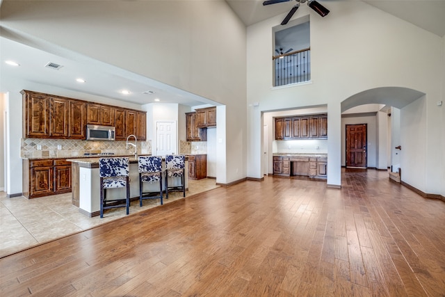 kitchen with ceiling fan, light wood-type flooring, a kitchen island with sink, high vaulted ceiling, and a breakfast bar area