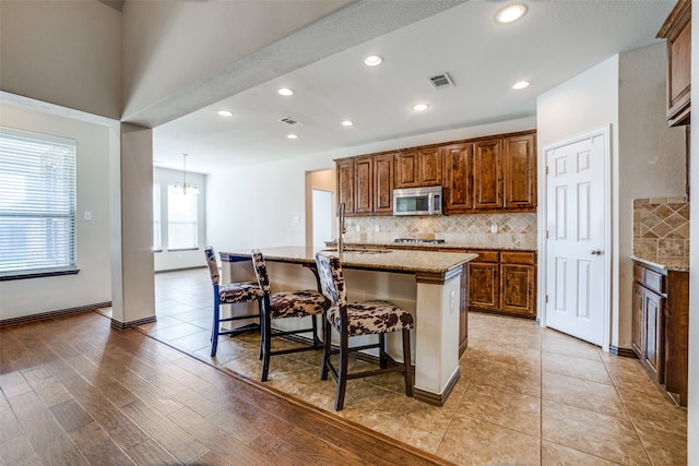 kitchen with an island with sink, decorative backsplash, sink, a kitchen breakfast bar, and light stone counters