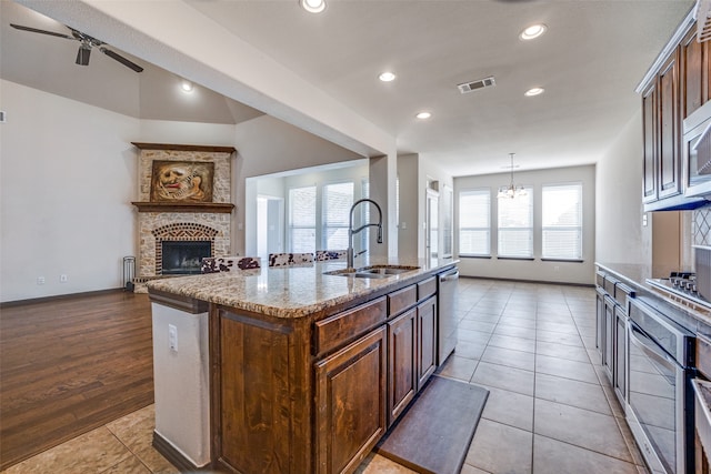 kitchen featuring a fireplace, light tile patterned floors, sink, pendant lighting, and an island with sink