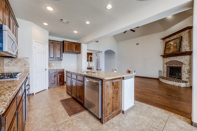 kitchen with sink, backsplash, light stone counters, a center island with sink, and stainless steel appliances