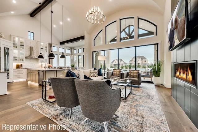 living room featuring light wood-style floors, a glass covered fireplace, a notable chandelier, and beamed ceiling