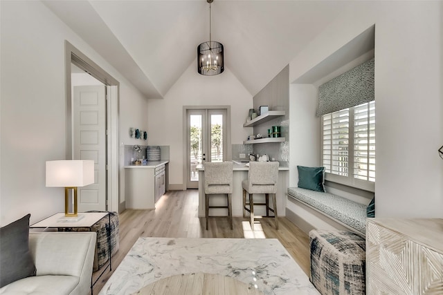 living room featuring vaulted ceiling, light hardwood / wood-style floors, french doors, and a chandelier