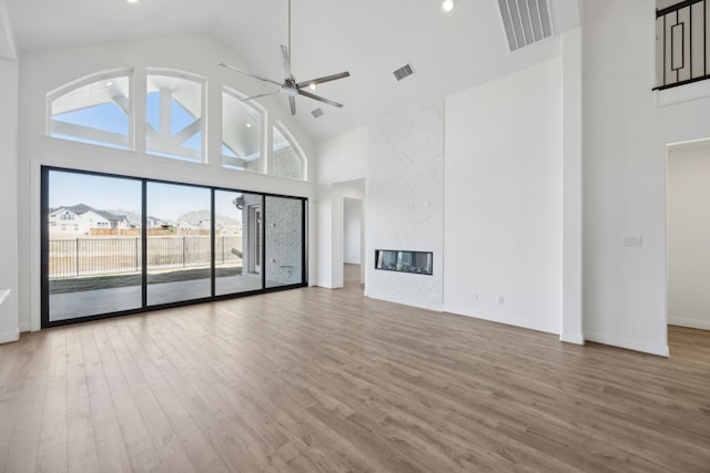 unfurnished living room with a ceiling fan, a high end fireplace, visible vents, and wood finished floors