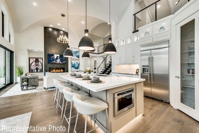 kitchen with a large fireplace, stainless steel built in refrigerator, pendant lighting, a kitchen island with sink, and white cabinets