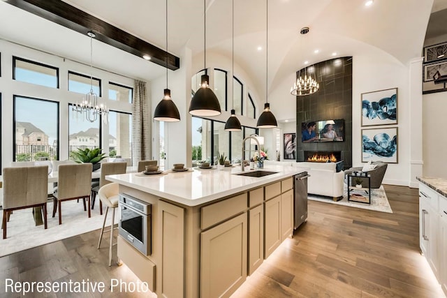 kitchen featuring stainless steel microwave, a large fireplace, hardwood / wood-style floors, an island with sink, and pendant lighting