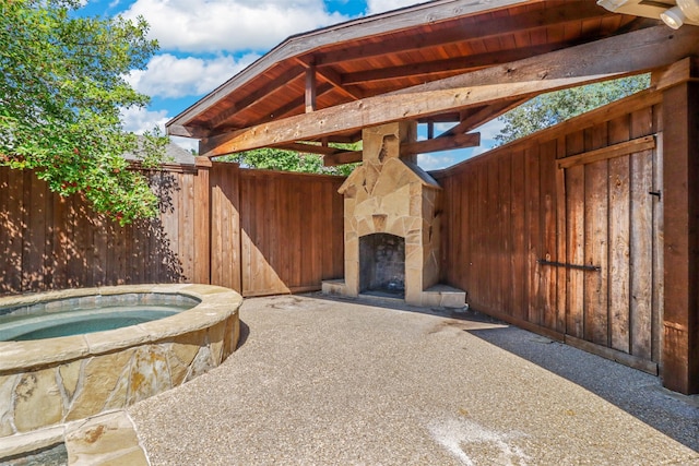 view of patio with an outdoor stone fireplace and an in ground hot tub