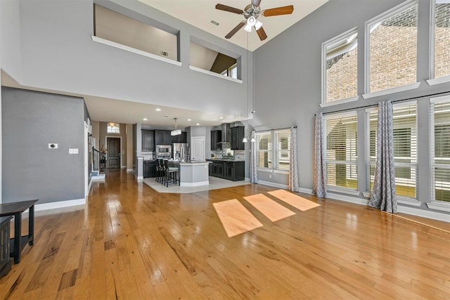 unfurnished living room featuring ceiling fan, light hardwood / wood-style floors, and a towering ceiling