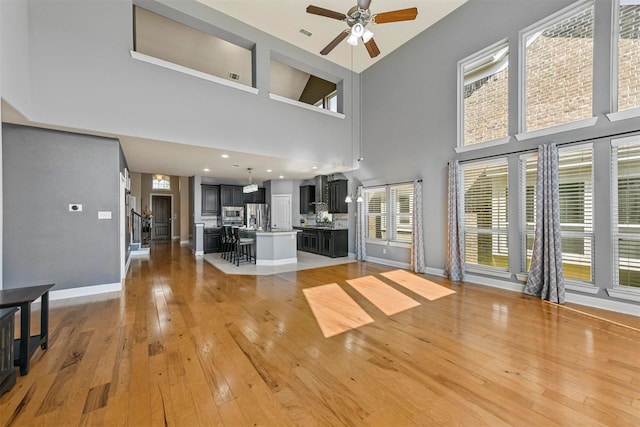 unfurnished living room with a ceiling fan, a towering ceiling, baseboards, light wood finished floors, and stairs