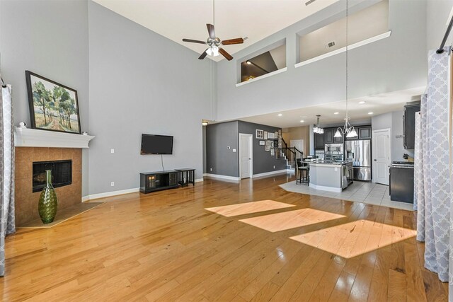 unfurnished living room featuring a tiled fireplace, a high ceiling, ceiling fan with notable chandelier, and hardwood / wood-style flooring