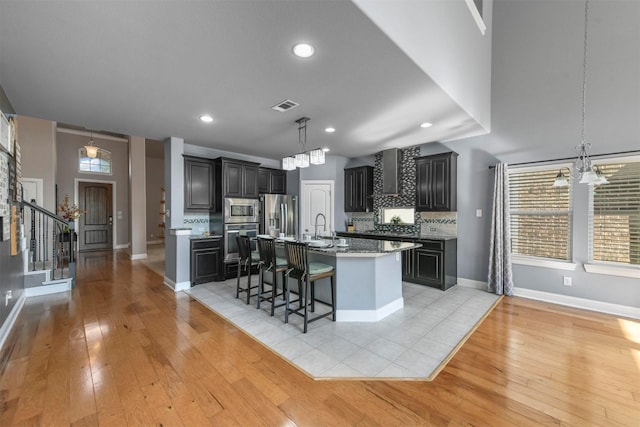 kitchen with backsplash, a center island with sink, a kitchen breakfast bar, light wood-type flooring, and stainless steel appliances