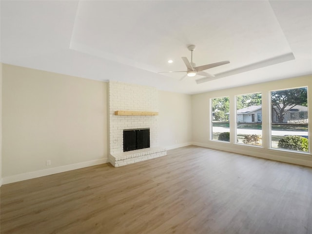 unfurnished living room with a tray ceiling, a fireplace, light wood-style flooring, and baseboards