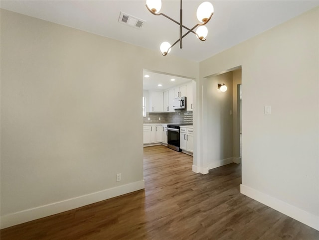 unfurnished dining area featuring dark wood-type flooring, an inviting chandelier, visible vents, and baseboards