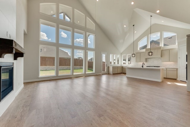 1029 Bleriot Dr, Fate, TX 75087 - unfurnished living room with high vaulted ceiling, a glass covered fireplace, a sink, light wood-type flooring, and recessed lighting