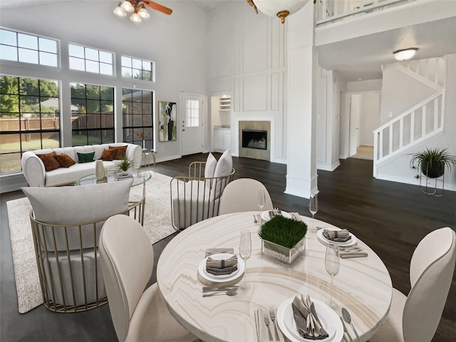 dining room featuring stairway, dark wood finished floors, a fireplace, and a towering ceiling